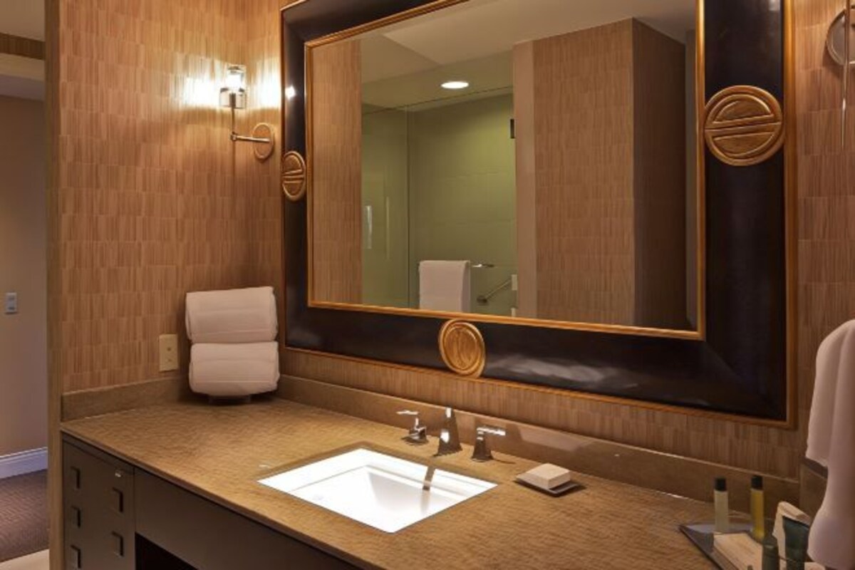 Un baño de hotel con un espejo grande, un lavamanos y un perchero para toallas.