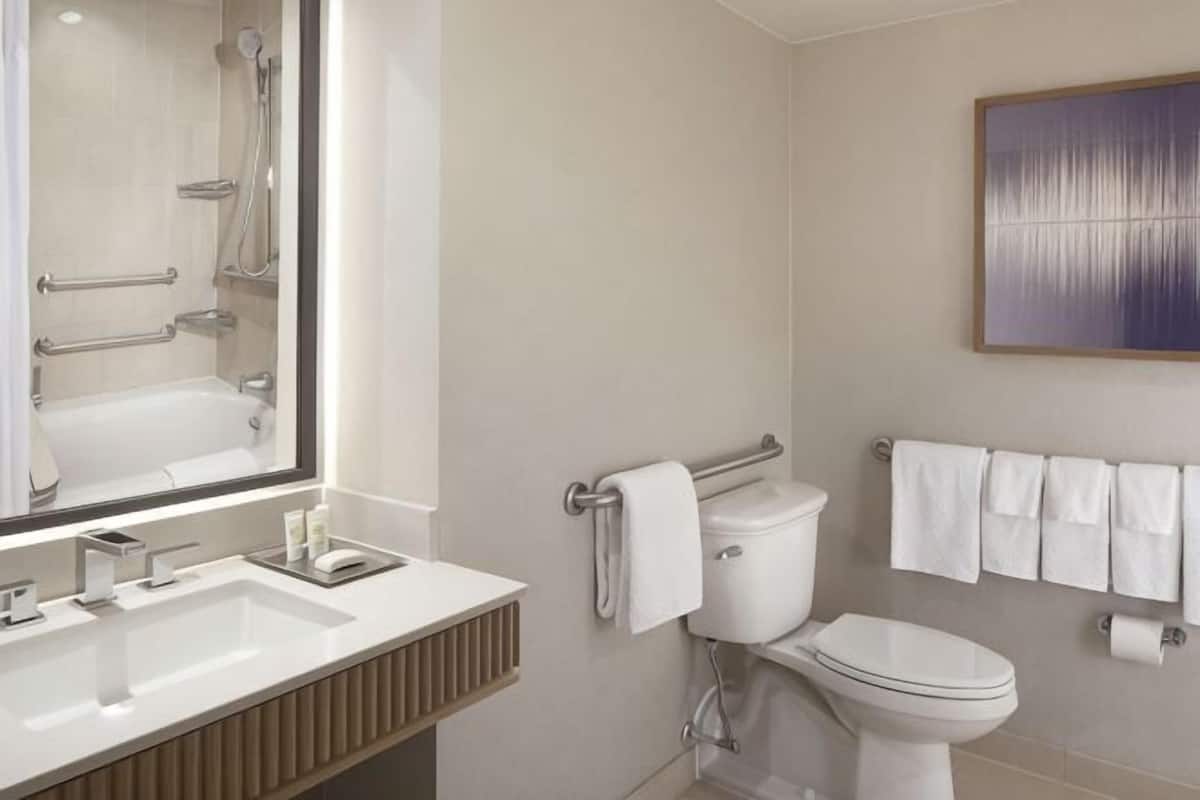 Une salle de bain moderne avec un grand miroir, une baignoire, des toilettes et un porte-serviettes.