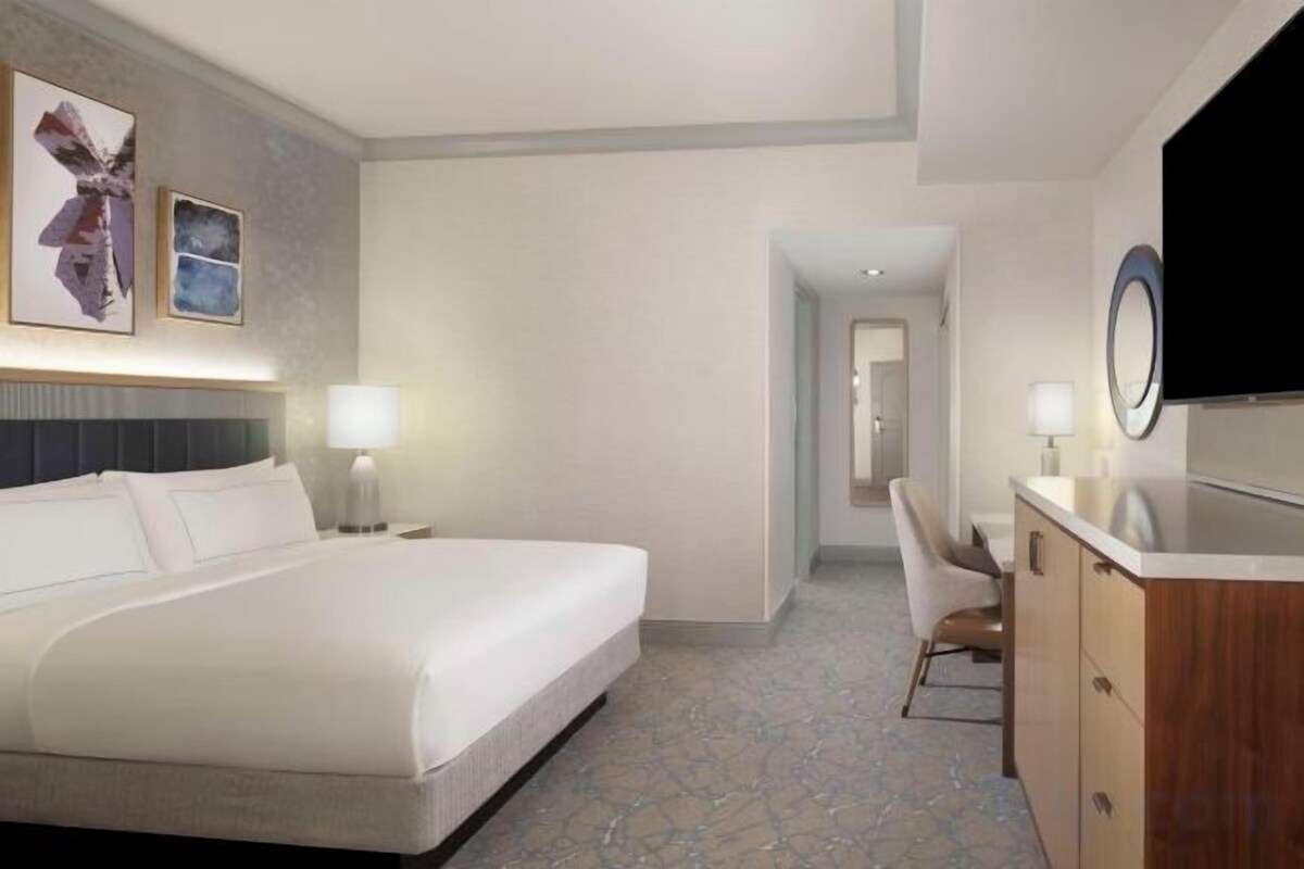 A hotel room with a large bed, a desk, a chair, and a television.