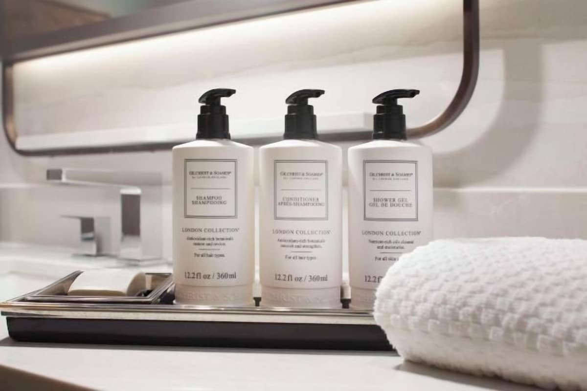 A bathroom with three bottles of shampoo and conditioner on a tray, a towel, and a mirror.