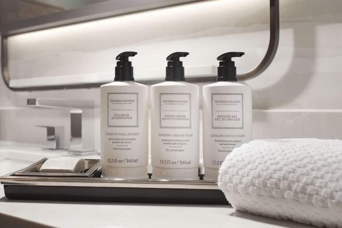 Trois flacons de produits de soins pour la peau sont posés sur le comptoir d’une salle de bain, à côté d’une serviette.