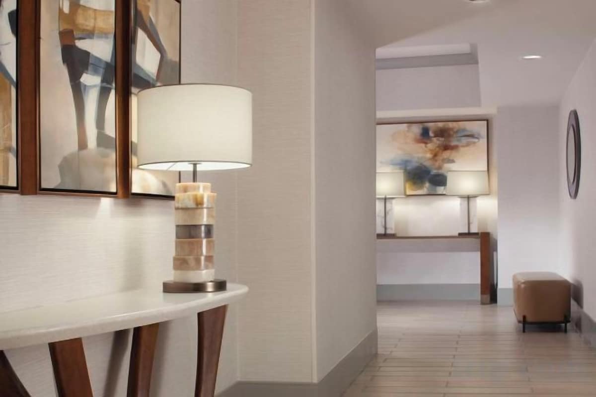 A modern hotel lobby with a white reception desk, a lamp, abstract art on the wall, and a seating area.