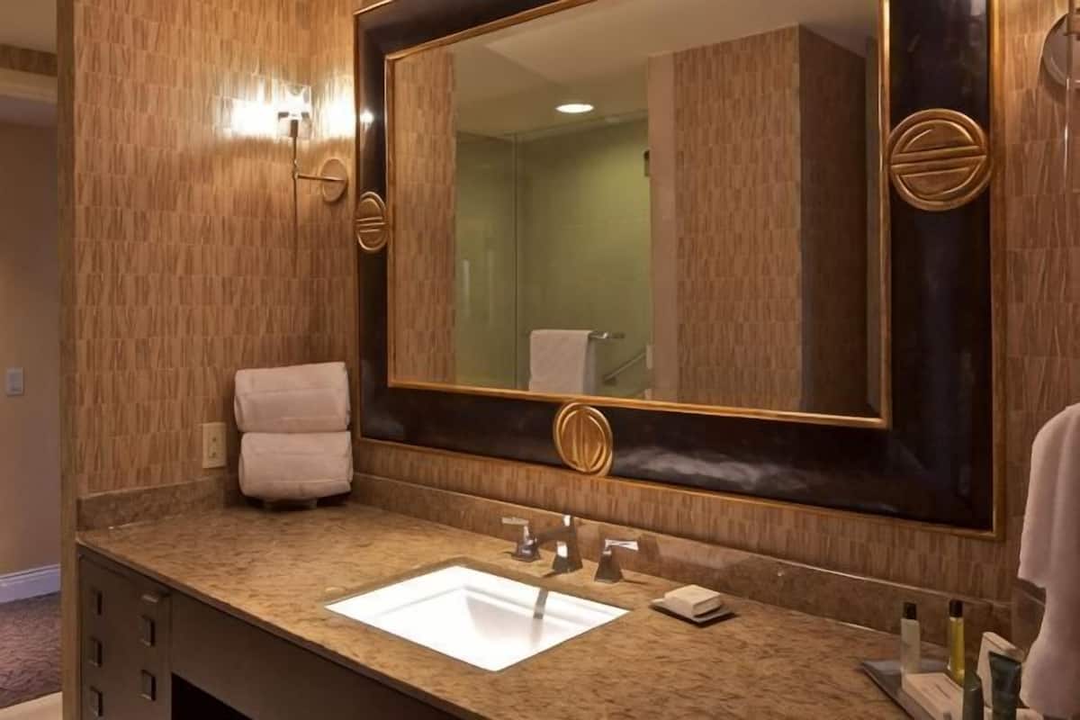 Une salle de bain avec un grand miroir, un lavabo, une serviette et un luminaire fixé au mur.