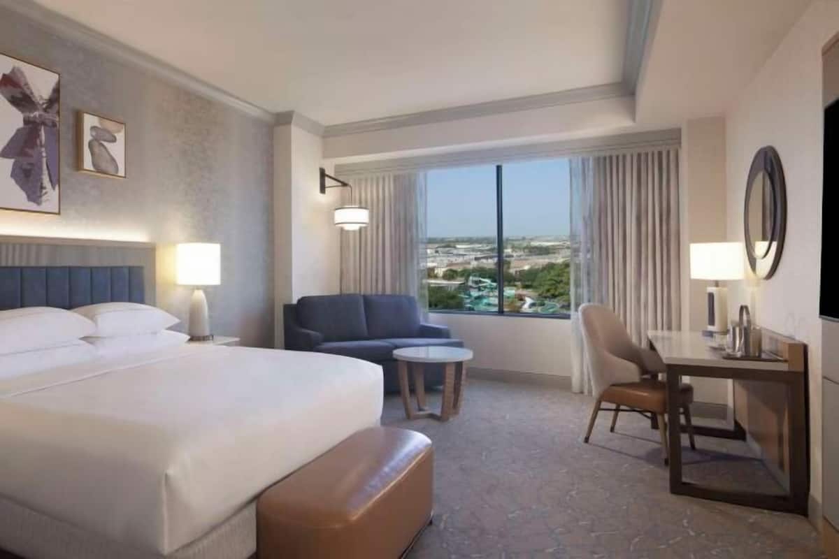 Une chambre d’hôtel avec un lit, un bureau, une chaise, une petite table et une vue sur la ville.