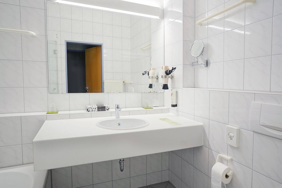 A modern bathroom with a white sink, mirror, and toilet paper dispenser.