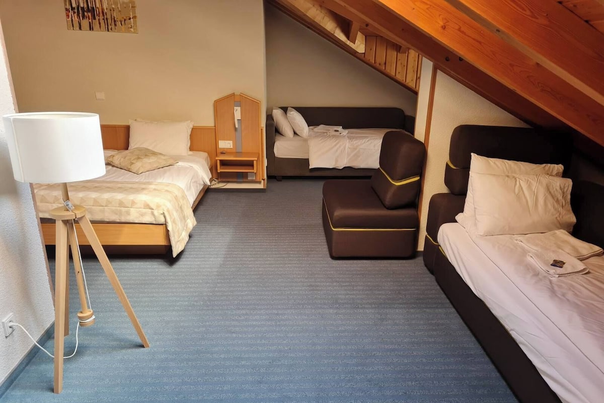 A compact hotel room with two beds, a small seating area, and a lamp.