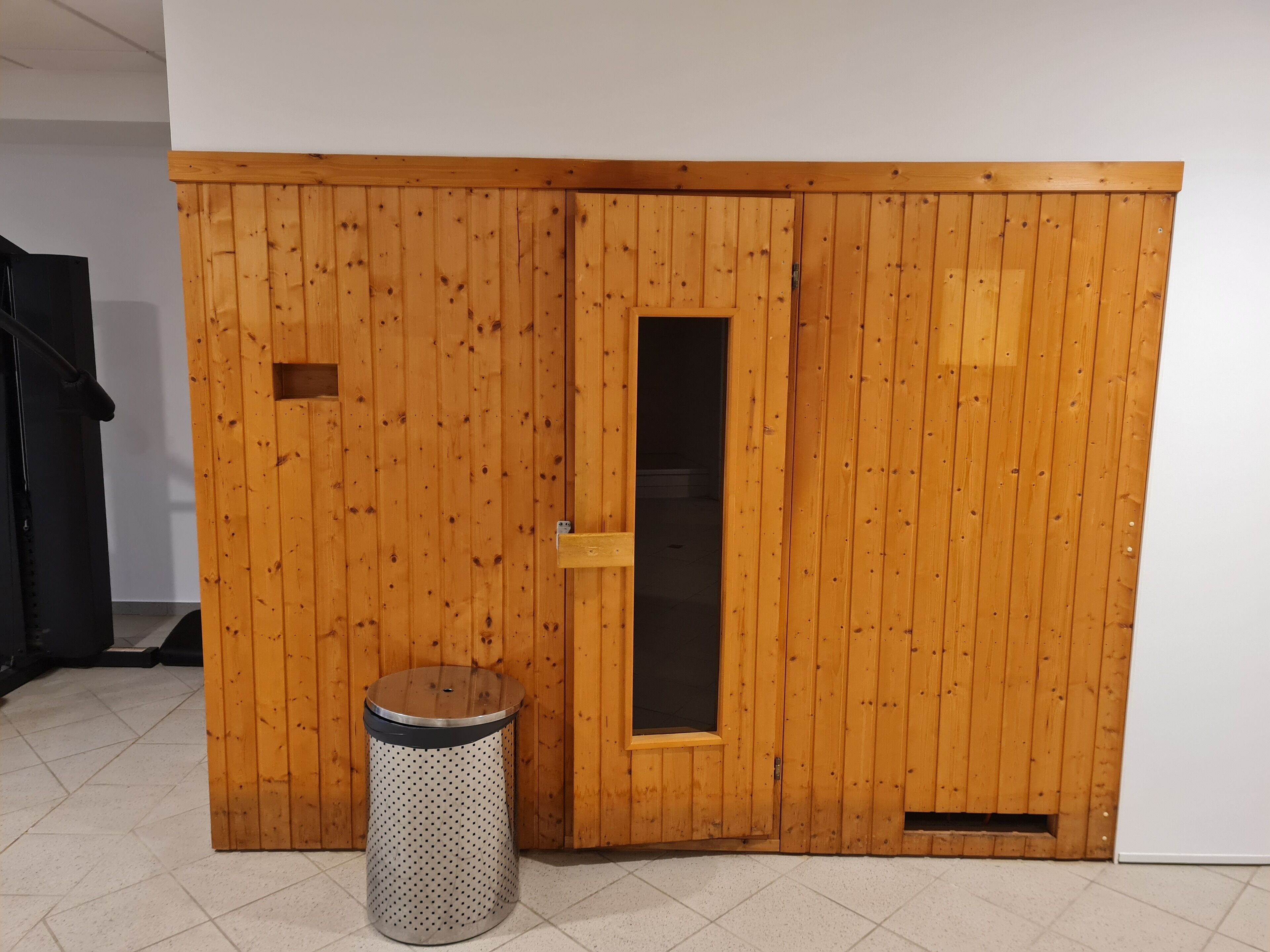 Quarto com guarda-roupa de madeira, um pequeno cesto de lixo e uma porta com janela.