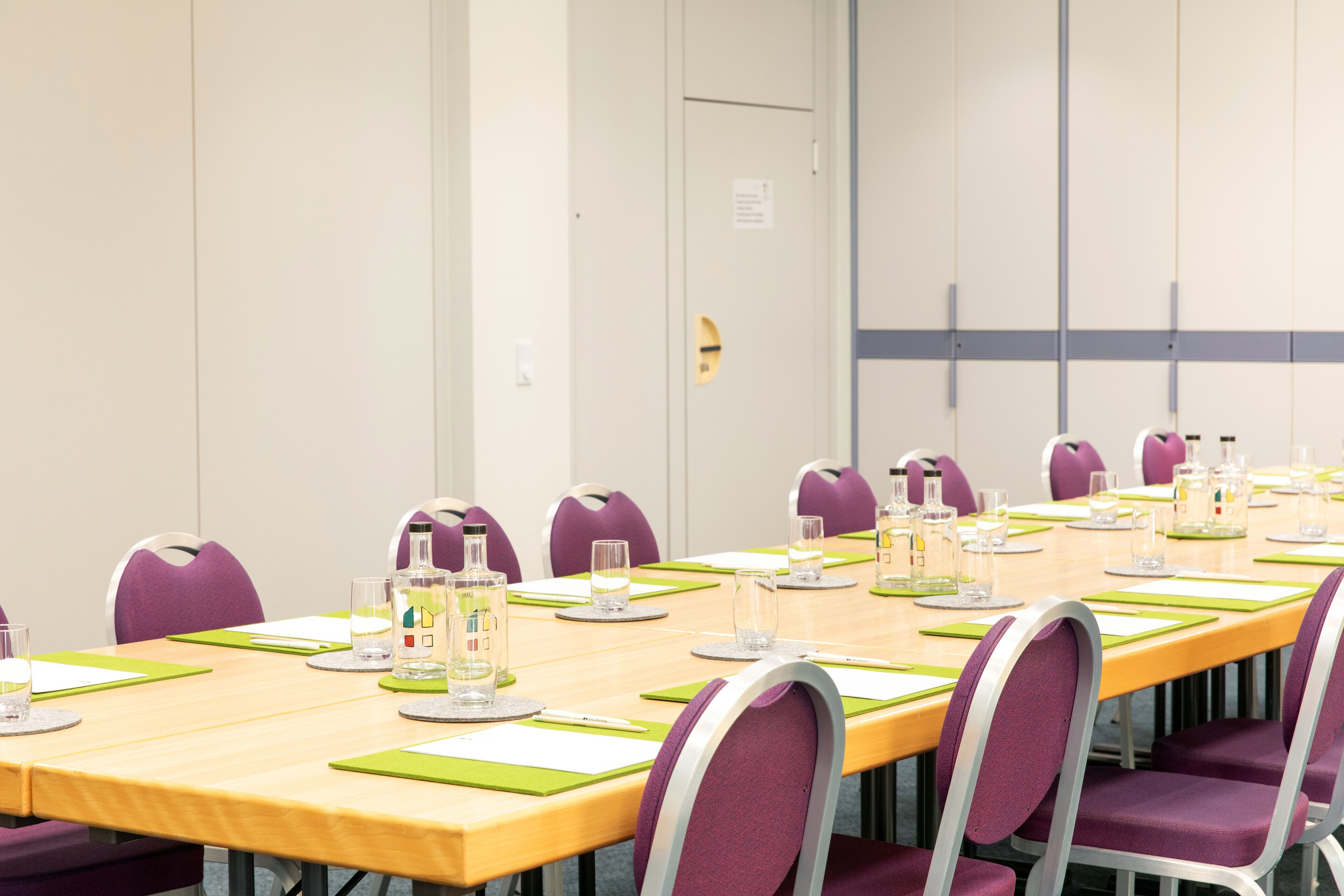 A conference room with a long table, purple chairs, and water glasses.
