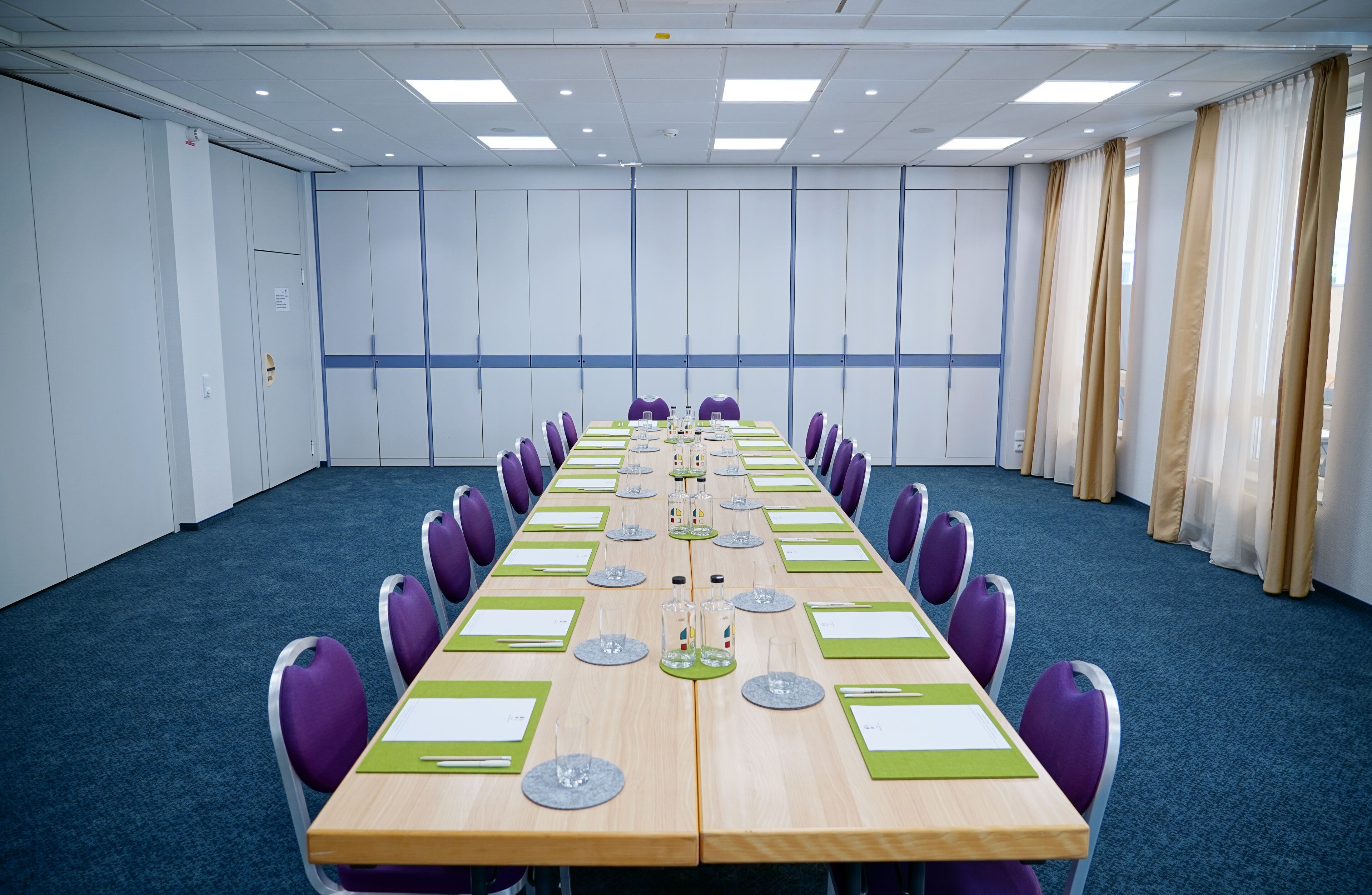 A conference room with a long table, purple chairs, and a blue carpet.