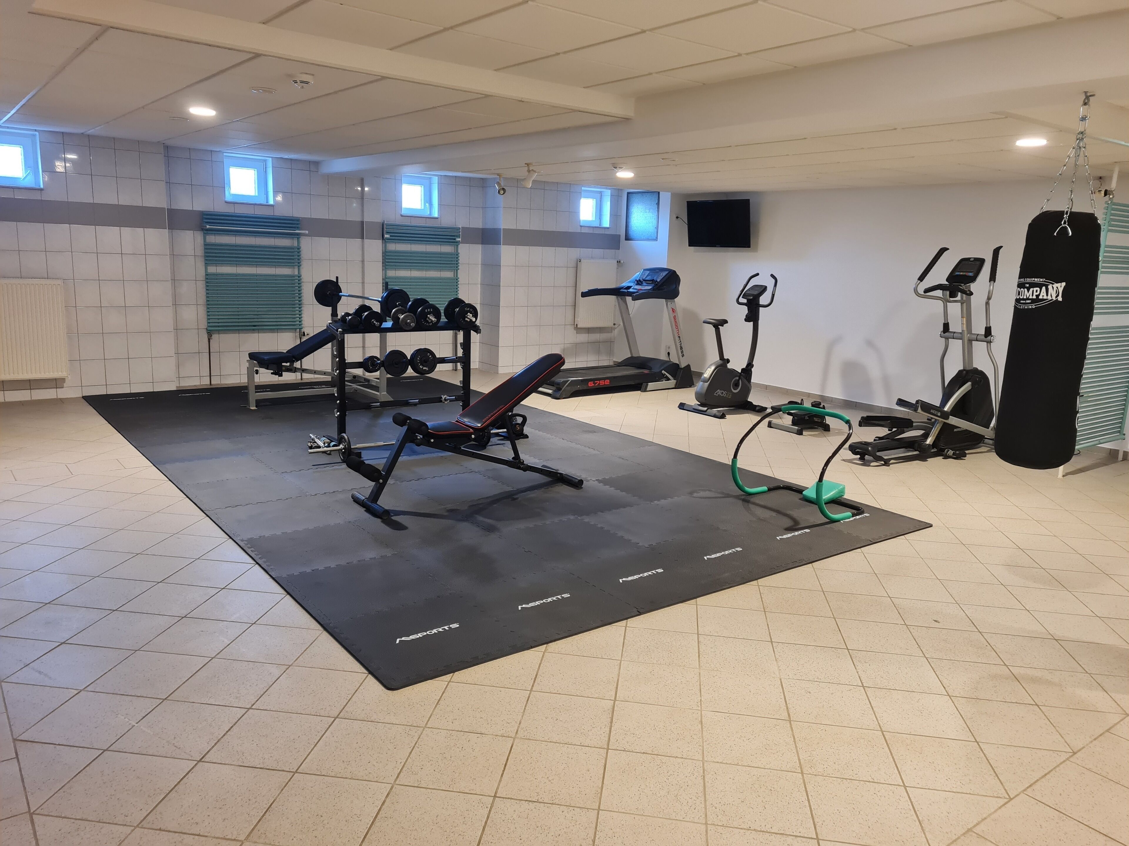 Un gimnasio con un banco de pesas, mancuernas, cintas de correr y un saco de boxeo.