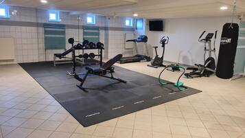 Een sportschool met een bankdrukapparaat, gewichten, loopbanden en een bokszak.
