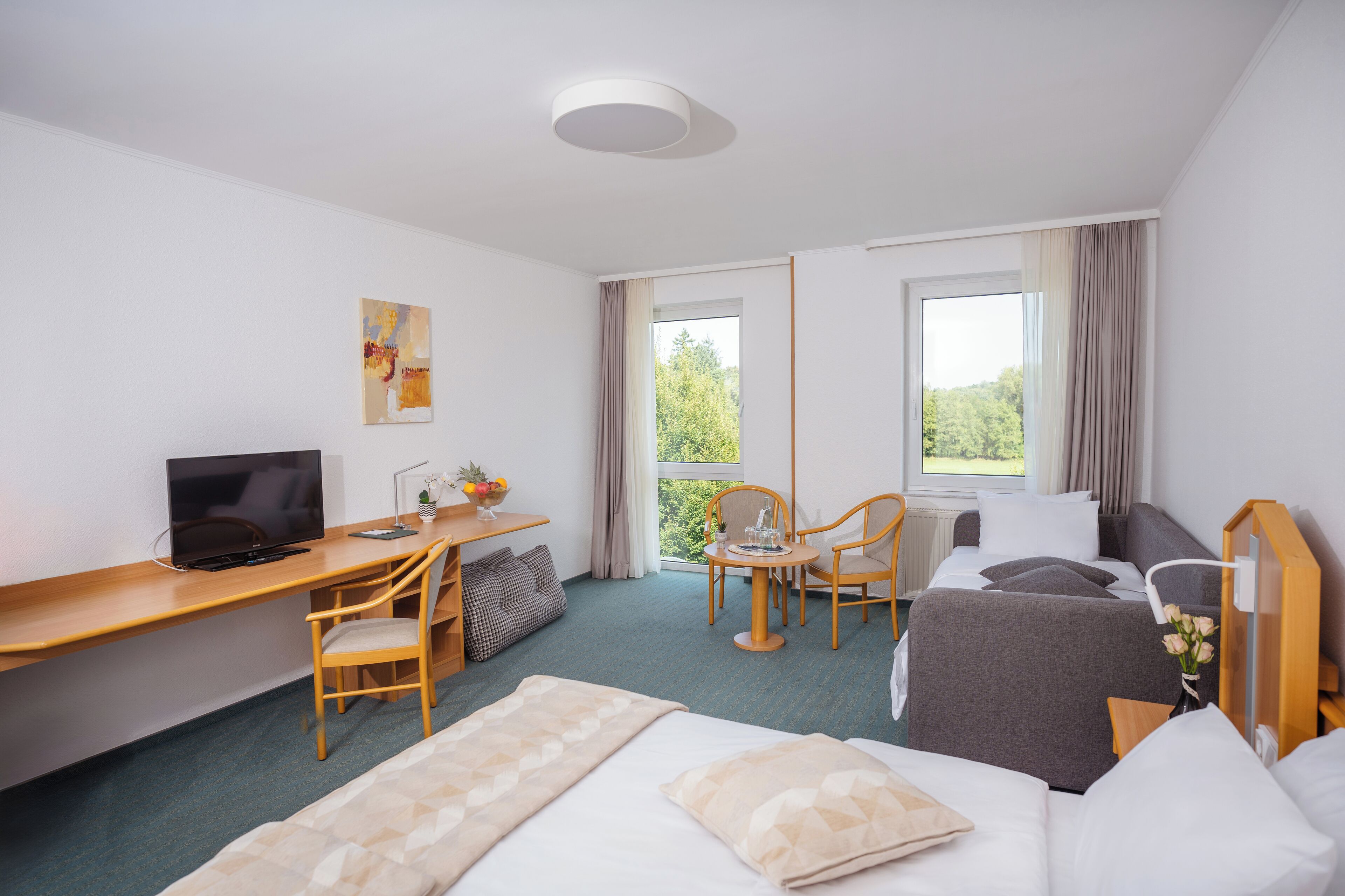A hotel room with a bed, desk, computer, chairs, and a window with curtains.