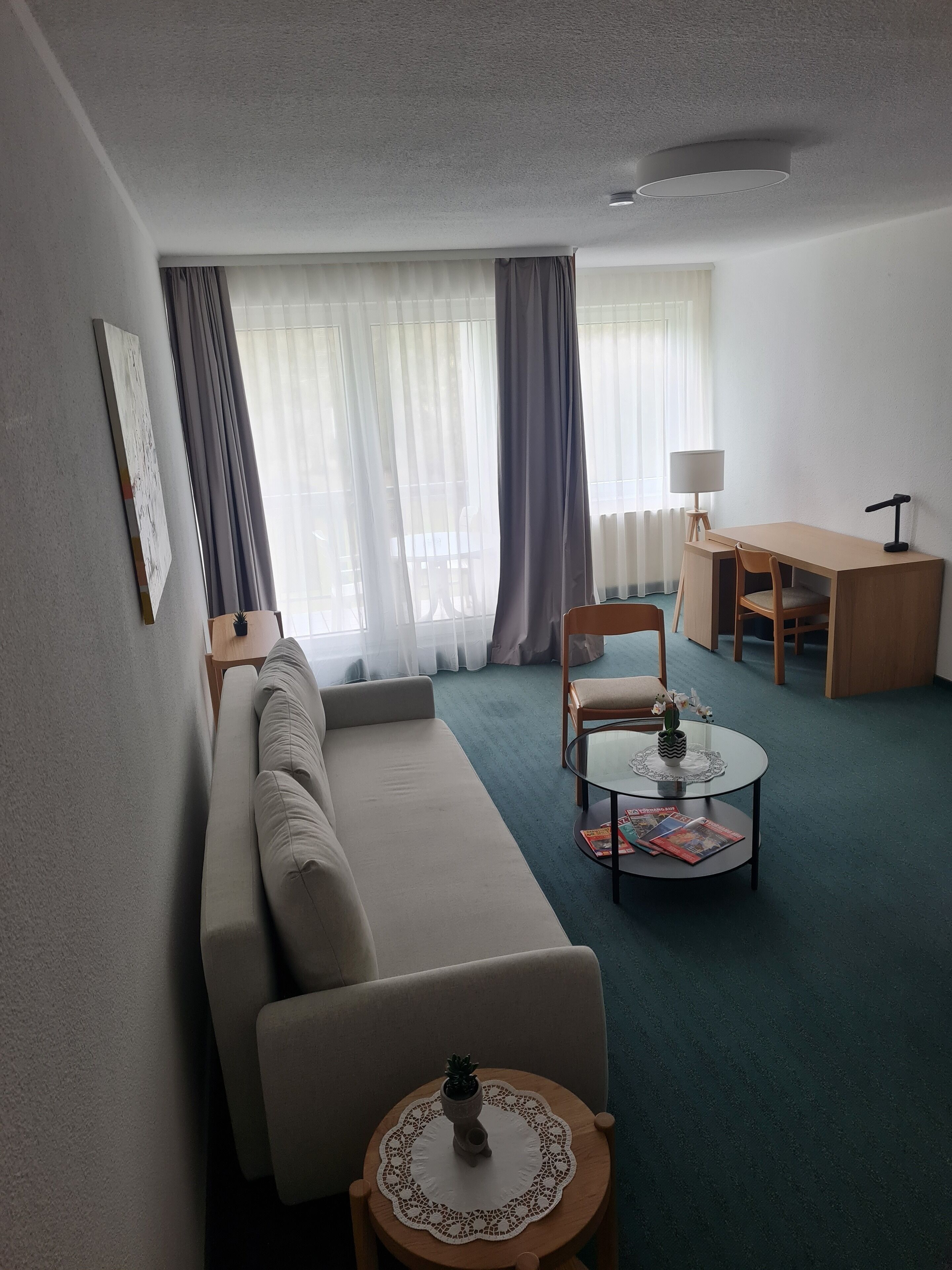 A living room with a sofa, a round coffee table, a small table with a lamp, and a desk with a chair.