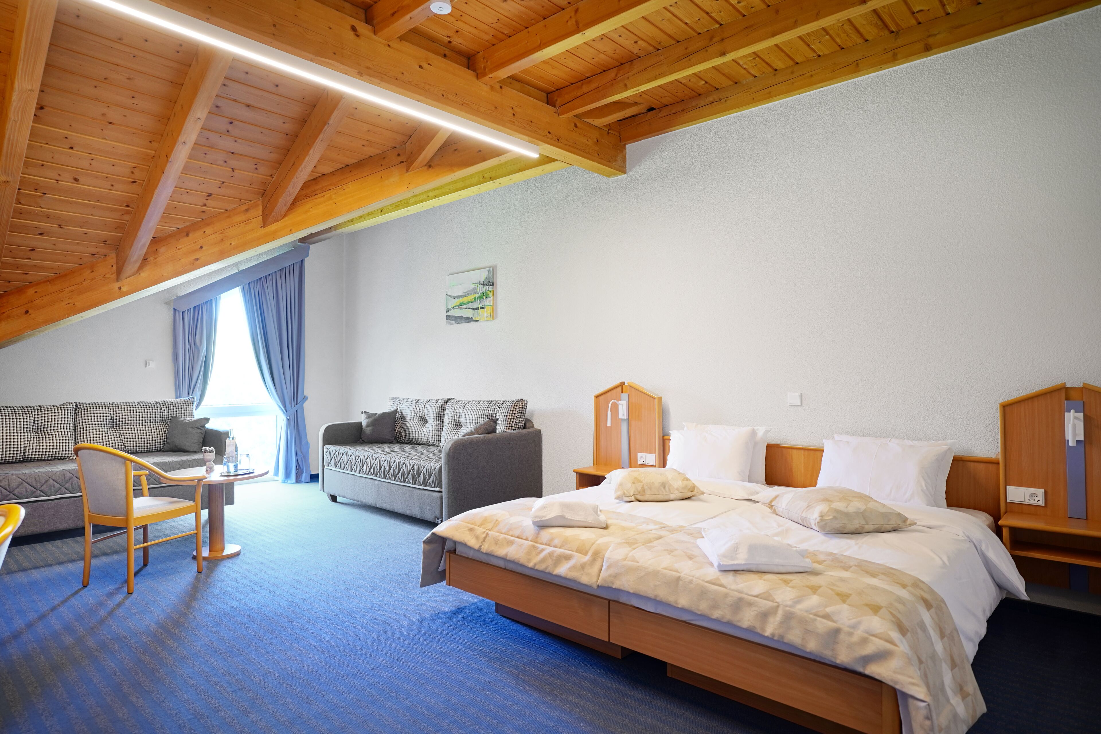 A bedroom with a wooden ceiling, a bed, a sofa, a chair, and a small table.