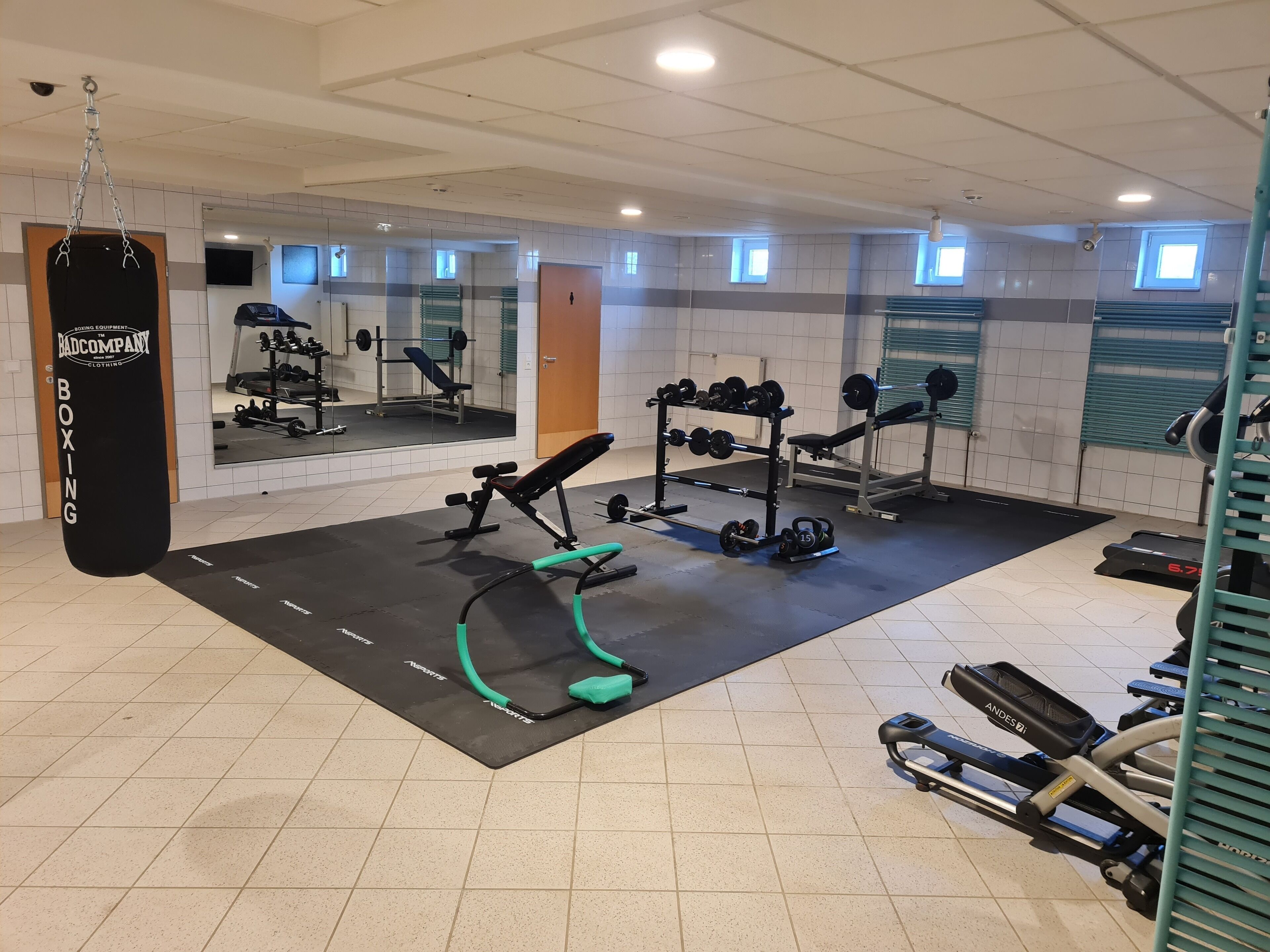 Un gimnasio con diverso equipo de ejercicio, incluyendo un saco de boxeo, bancos de pesas y una caminadora.
