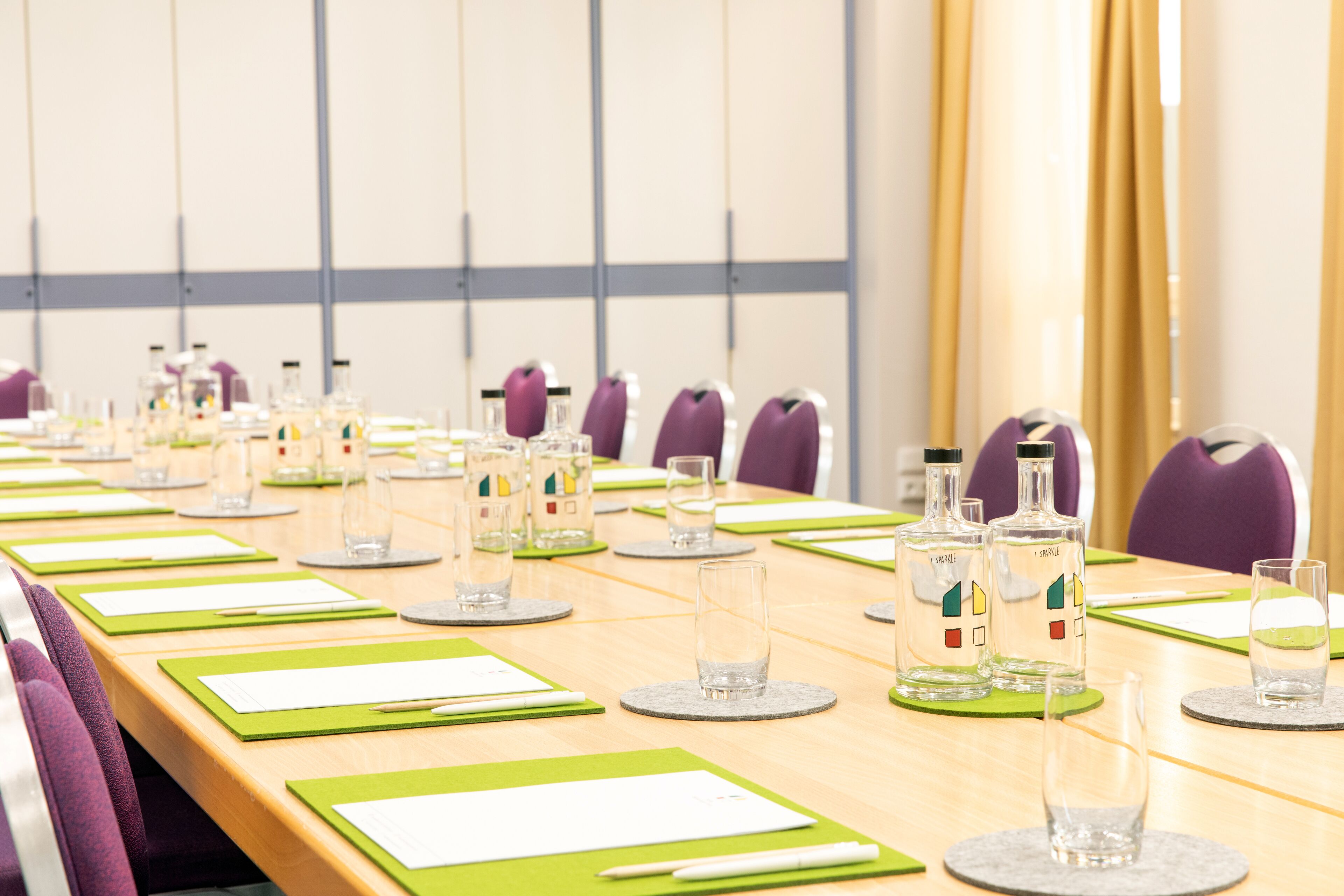 A conference room with a long table, green placemats, and purple chairs.