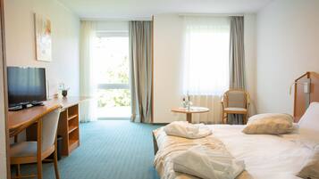 Een hotelkamer met een bed, een bureau met een televisie, een stoel en een kleine tafel met een plant.