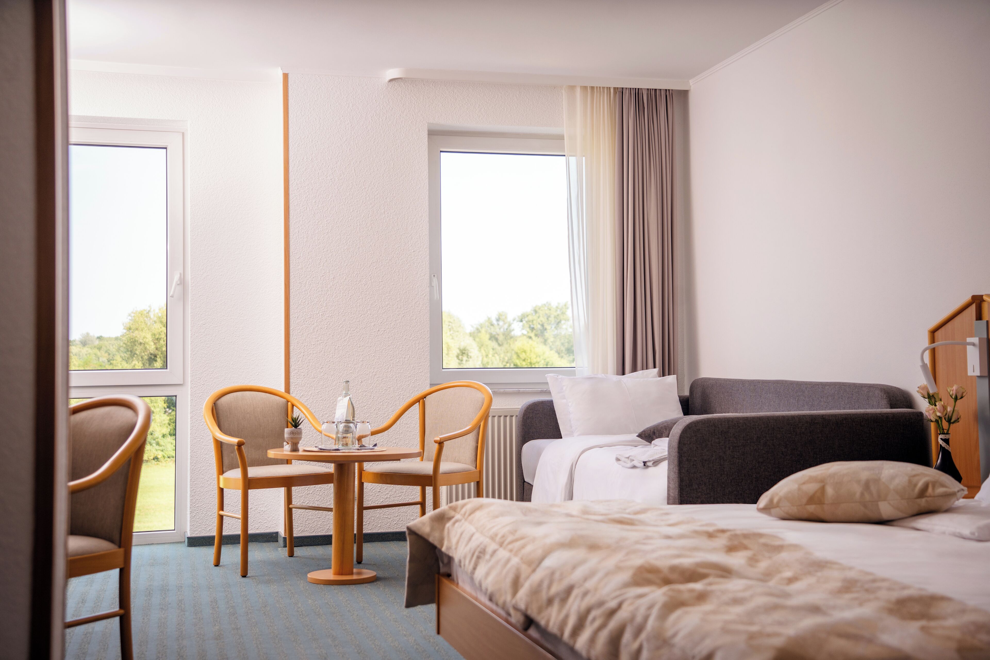 Ein Hotelzimmer mit einem Bett, einer Couch, einem Tisch mit Stühlen und einem Fenster mit Vorhängen.