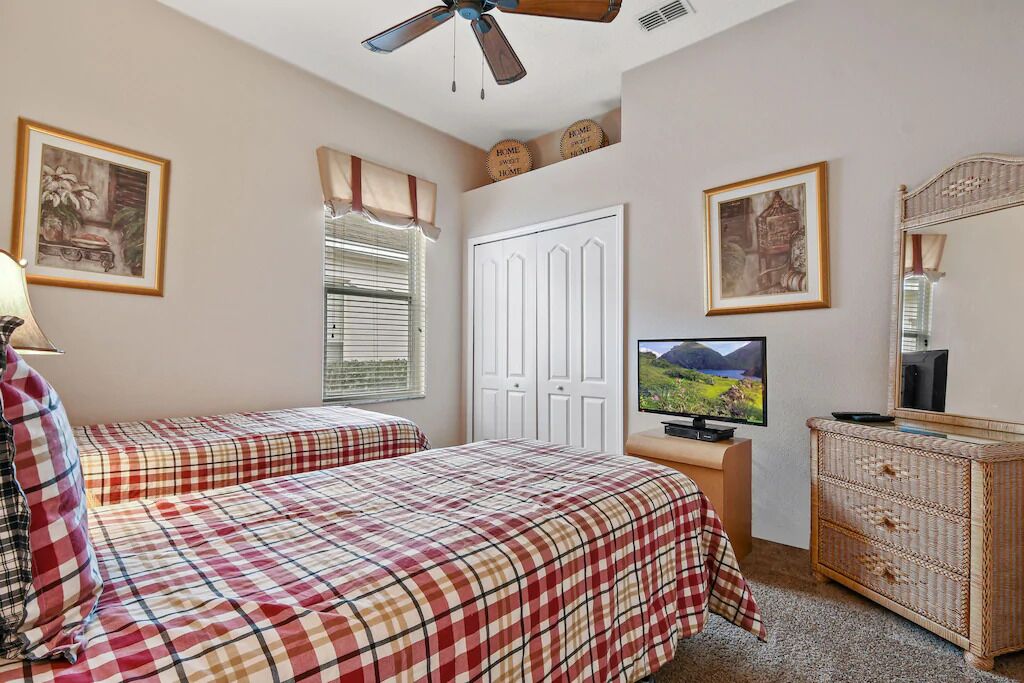 A bedroom with two beds, a television, a dresser, and a ceiling fan.