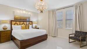 Um quarto espaçoso com uma cama grande, duas mesas de cabeceira com luminárias, um lustre moderno e uma janela com cortinas.