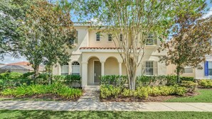 A two-story house with a beige facade, a tiled roof, and a front entrance with a door. - Mediterranean Style Family Villa Close To Disney (Kissimmee)