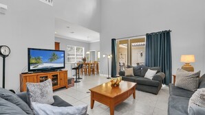 A spacious living room with a flat-screen TV, a wooden coffee table, and a sofa. A dining area with a table and chairs is visible in the background. - Mediterranean Style Family Villa Close To Disney (Kissimmee)