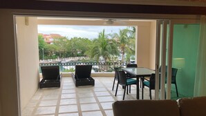 Un balcone con tavolo e sedie, un divano e vista su una piscina e palme.