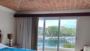 Una camera d'albergo con un letto, un comodino, una lampada, una sedia e vista su un porto turistico attraverso una porta scorrevole in vetro.