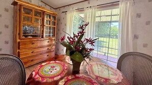 Un comedor con un mueble de madera, una mesa con posavasos florales y un jarrón con flores rojas.