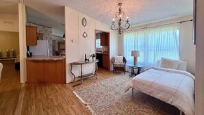 Un dormitorio con cama, una silla, una mesa, una araña y vistas a una cocina y un baño.