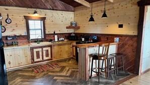 A rustic kitchen with wooden walls, a herringbone floor, a bar area, and a window with blinds.
