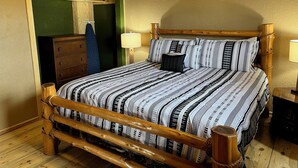 A wooden bed with a patterned bedspread and pillows, a wooden dresser, and two bedside lamps in a room with green walls and wooden flooring.