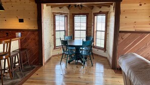 A wooden interior with a dining table and chairs, large windows, and a wooden ceiling.
