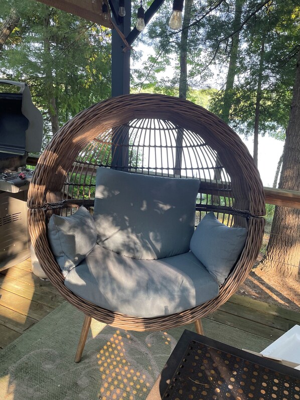 A wicker hanging chair with cushions, a grill, and a wooden deck. - Traverse City LAKE Front Cottage15 Min to Downtown Front St. PET Friendly GRILL (Traverse City)