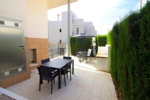 Une terrasse avec une table et des chaises, un barbecue et une haie.