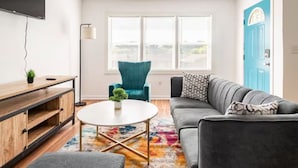 Een moderne woonkamer met een grijze bank, een blauwgroene fauteuil, een ronde salontafel en een televisie op een houten dressoir.