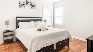 Een slaapkamer met een donker houten bed, wit beddengoed, een nachtkastje met een lamp en kunst aan de muur.