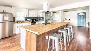 Een moderne keuken met witte kasten, een houten kookeiland met barstoelen, roestvrijstalen apparatuur en een blauwe deur op de achtergrond.