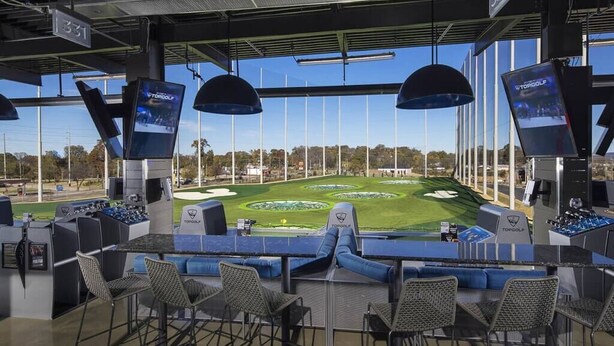 Een tribune voor golf met zitplaatsen en schermen waarop een golfbaan te zien is.