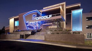 Een modern gebouw met een opvallend 'TopGolf' bord, met een gestileerd golfclub logo.