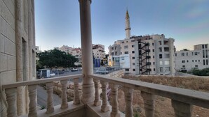 Ein Balkon mit Blick auf eine Stadtlandschaft, darunter eine Moschee mit Minarett, moderne Gebäude und eine Straße mit Fahrzeugen.