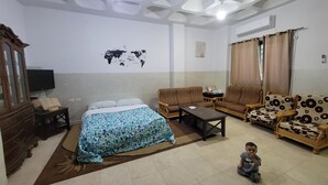 Ein Wohnzimmer mit einem Bett, Sofas, einem Couchtisch und einer Weltkarte an der Wand, sowie einem spielenden Kind.