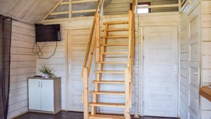 A wooden ladder leading to a lofted area in a cabin with a white cabinet and a plant.