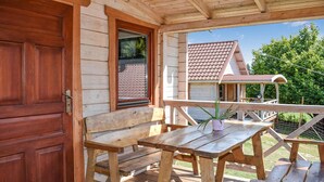 A wooden deck with a bench and table, a door, and a view of a house with a tiled roof.