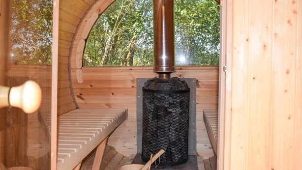 A sauna room with a wooden interior, a central heating element, and a wooden bucket.