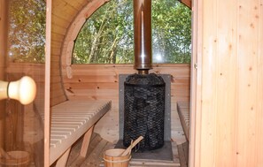 Un sauna avec un intérieur en bois, un élément chauffant central et un seau en bois.