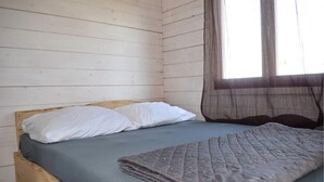 A single bed with a blue mattress and a grey quilt, white pillows, and a wooden headboard.