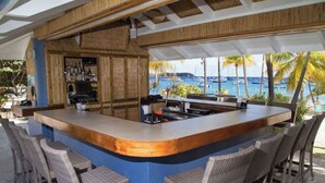 Eine Bar mit einer gebogenen Theke, Barhocker und Blick auf das Meer mit Booten.