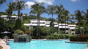 Ein Pool mit Wasserspiel, umgeben von Palmen und Hotelgebäuden.