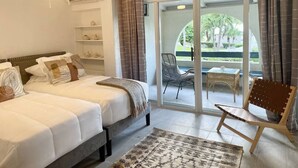 Ein Schlafzimmer mit zwei Betten, einem Deckenventilator, einem großen Fenster mit Vorhängen und Blick ins Freie.